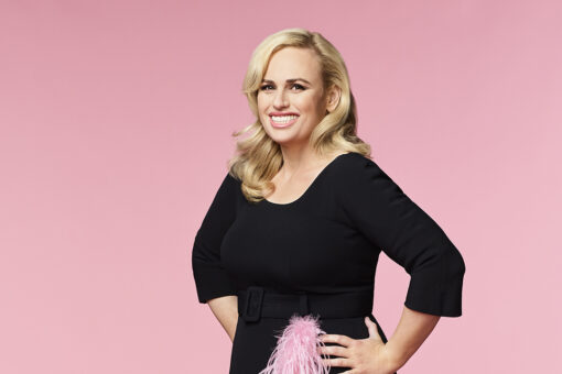Rebel Wilson power poses in zip-up swimsuit on beach